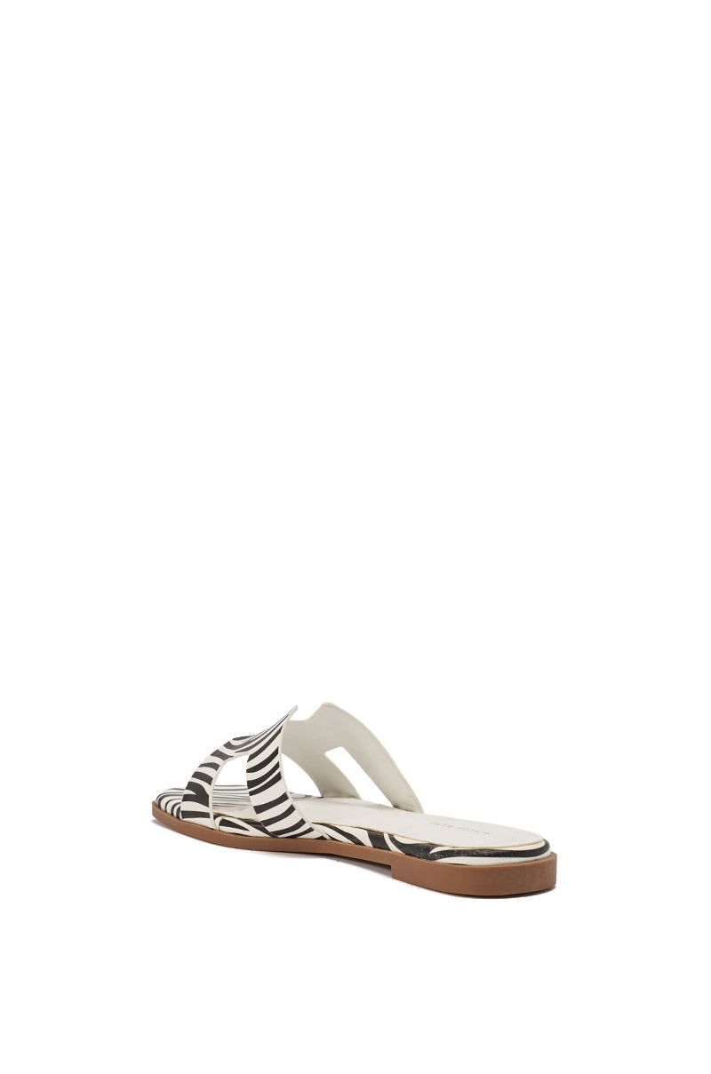 The AKIRA HOWDY ZEBRA SLIP ON FLAT SANDAL features a brown sole, white footbed, and black-and-white zebra-striped cut-out upper straps, shown from a rear side angle against a white background. 6