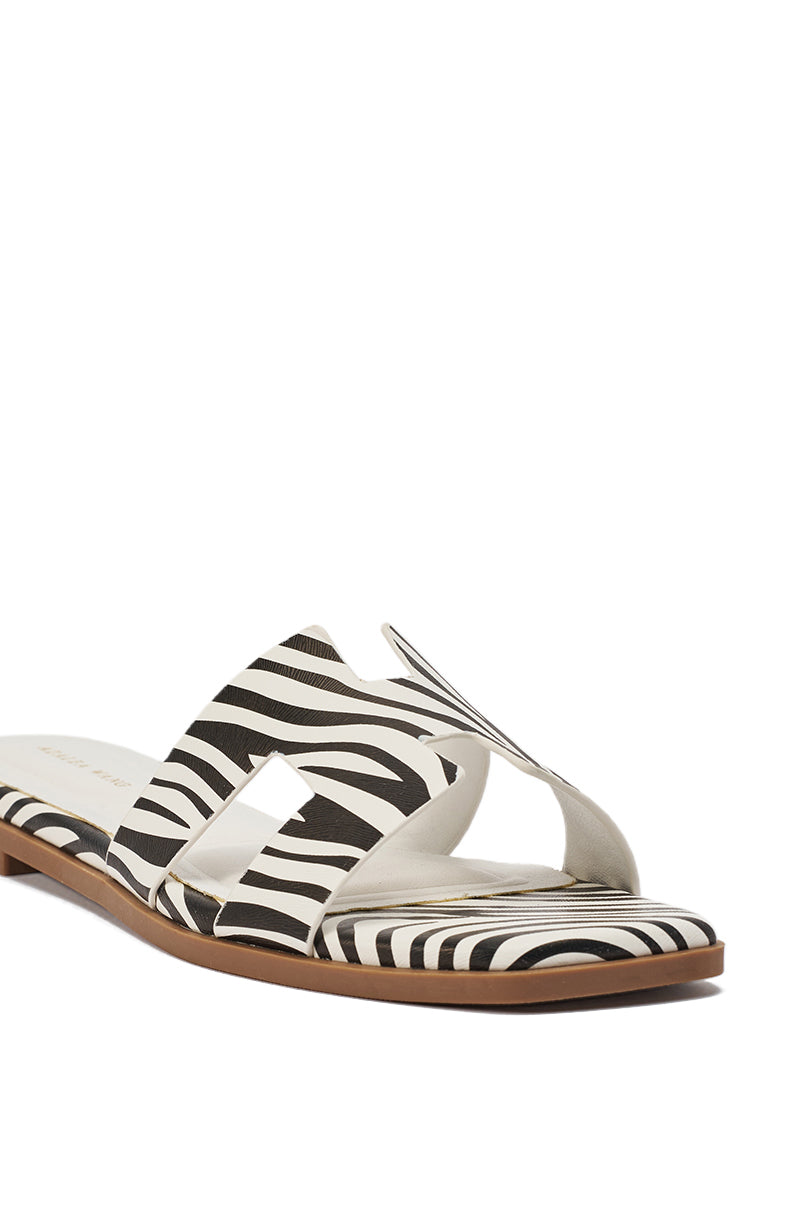 The AKIRA HOWDY Zebra Slip On Flat Sandal features black and white zebra-print cut-out straps and a brown sole, offering bold style. Shown on a white background. 7