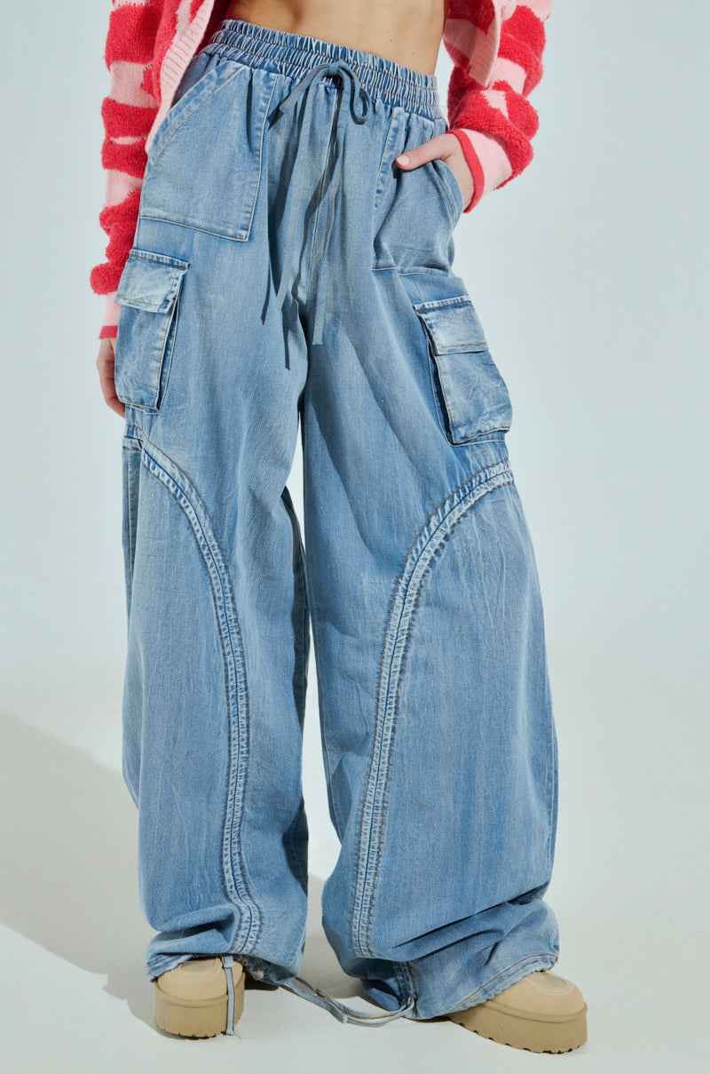 Someone wearing light blue MIA FLOW PANT high-rise relaxed fit cargo jeans with multiple pockets is paired with a pink and white striped top. They're on a light background and wearing beige shoes.