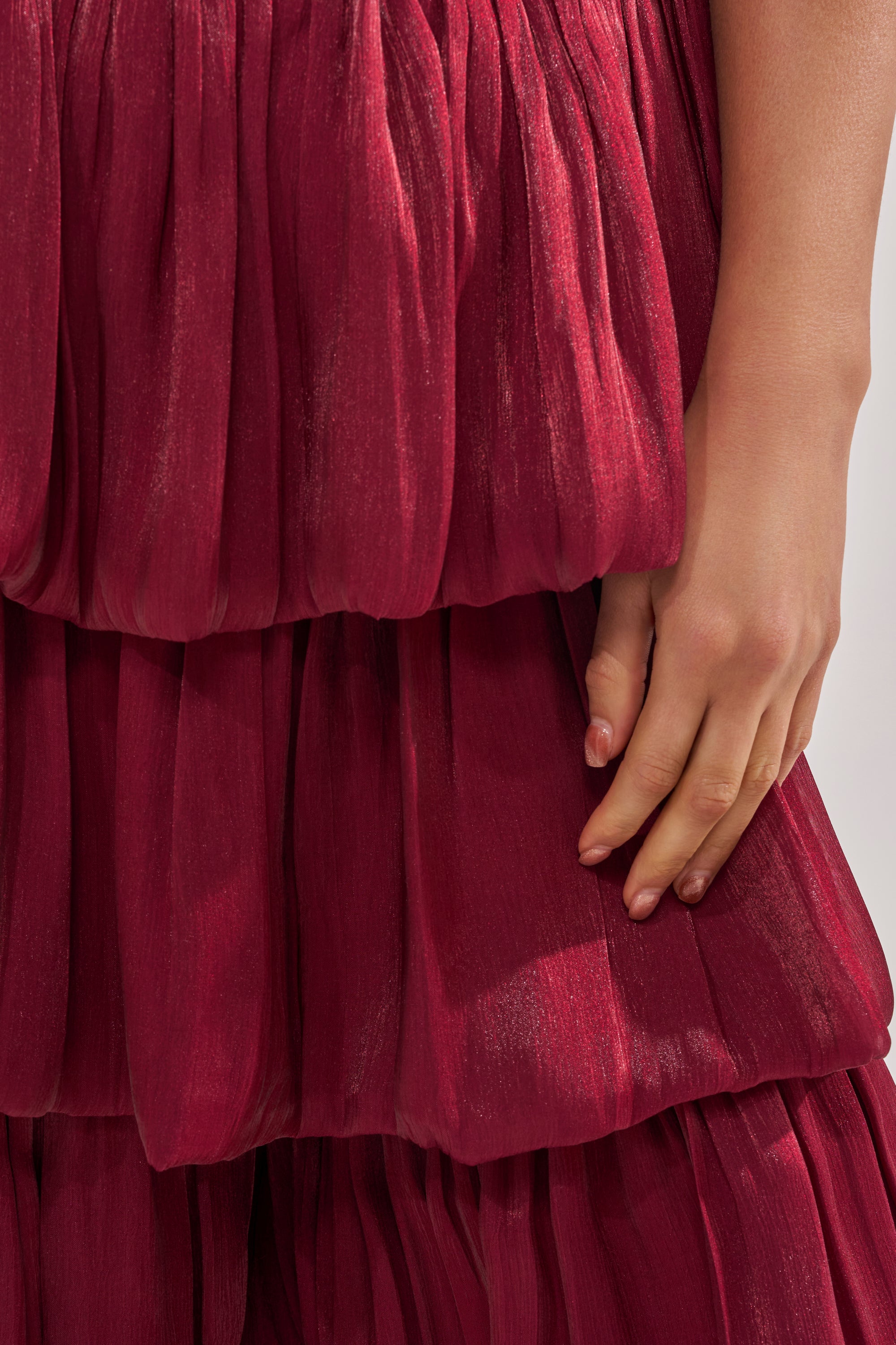 A close-up shows a hand resting on the STAR OF THE NIGHT FLOUNCY PANT IN BURGUNDY, featuring voluminous pleats and chiffon-like, slightly shiny fabric, with only part of the arm and lower half of the pants visible. 10