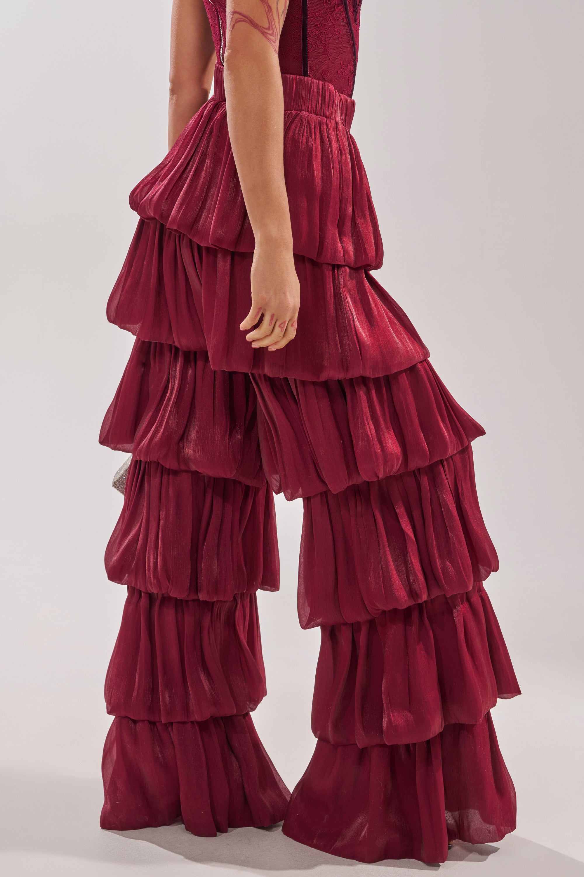 Someone wears the STAR OF THE NIGHT FLOUNCY PANT IN BURGUNDY—deep red, voluminous high-rise pants with shimmery, dramatic ruffle tiers from waist to hem—for a bold and striking fashion statement. 5