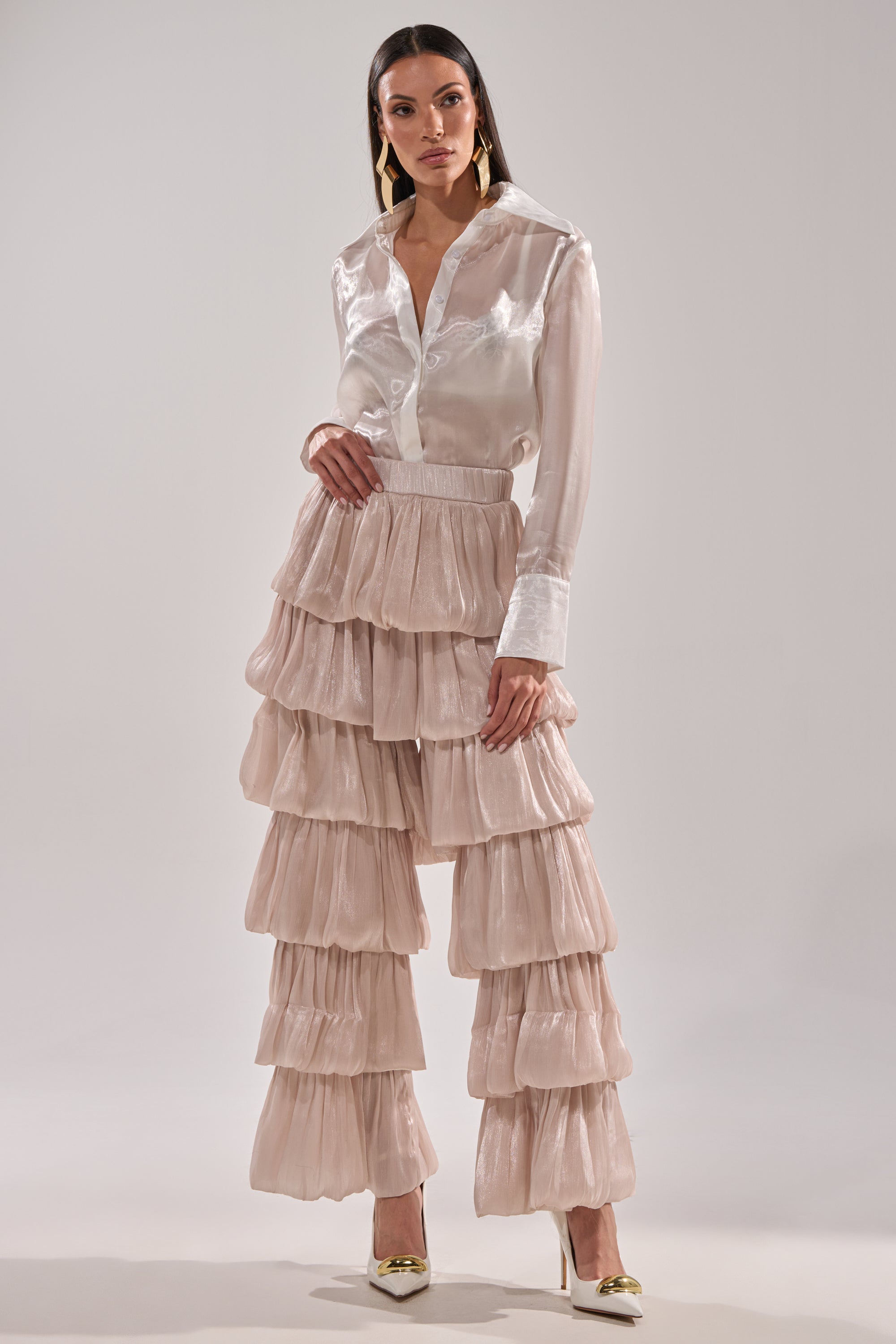 A woman wears a shiny white button-up blouse with long sleeves and the STAR OF THE NIGHT FLOUNCY PANT IN IVORY. She stands in high heels against a plain light background, looking confidently at the camera. 5