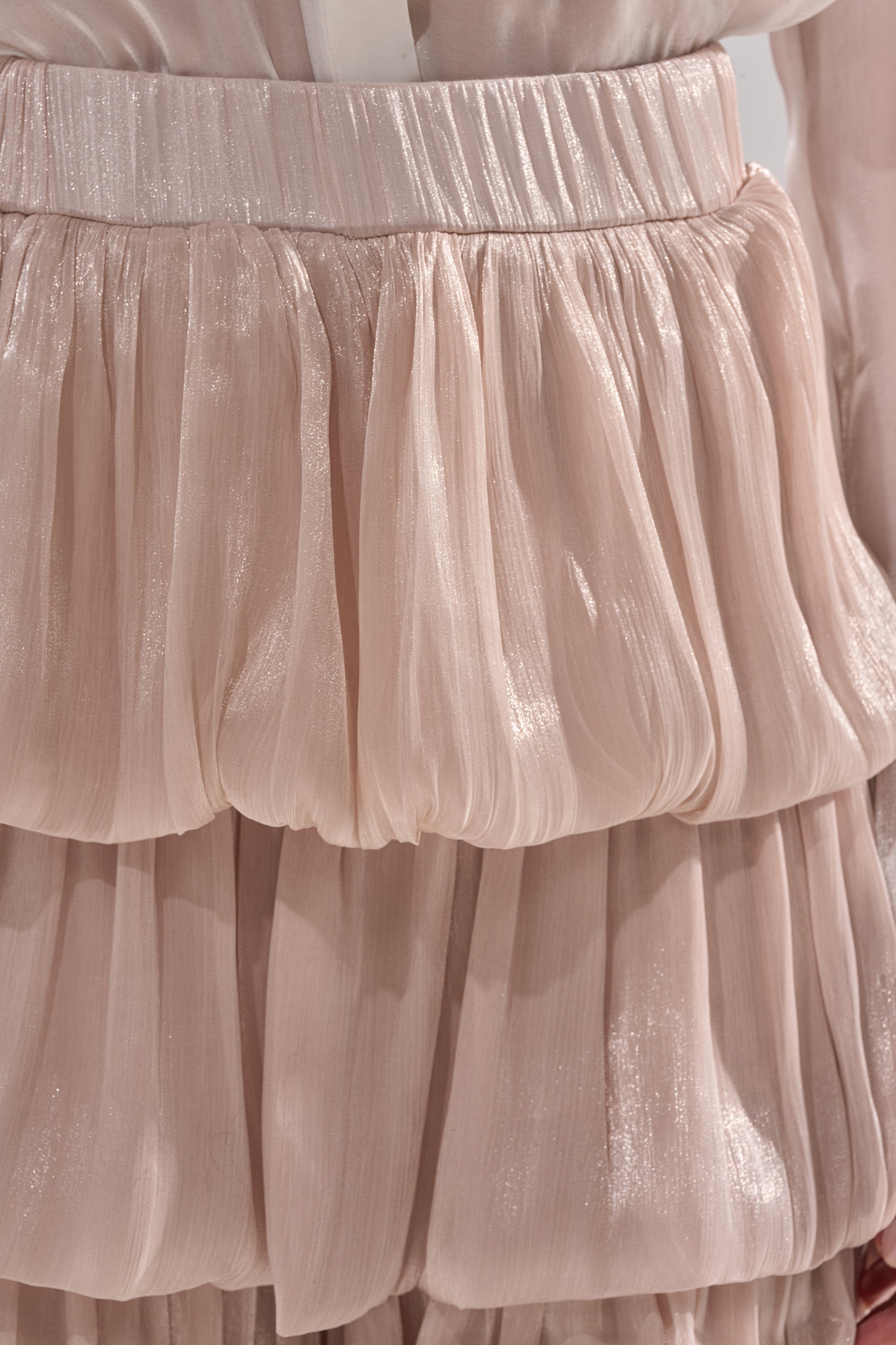 Close-up of the STAR OF THE NIGHT FLOUNCY PANT IN IVORY, made of shimmery, light pink sheer fabric with gathered and layered ruffles for a flouncy silhouette reminiscent of organza. 7