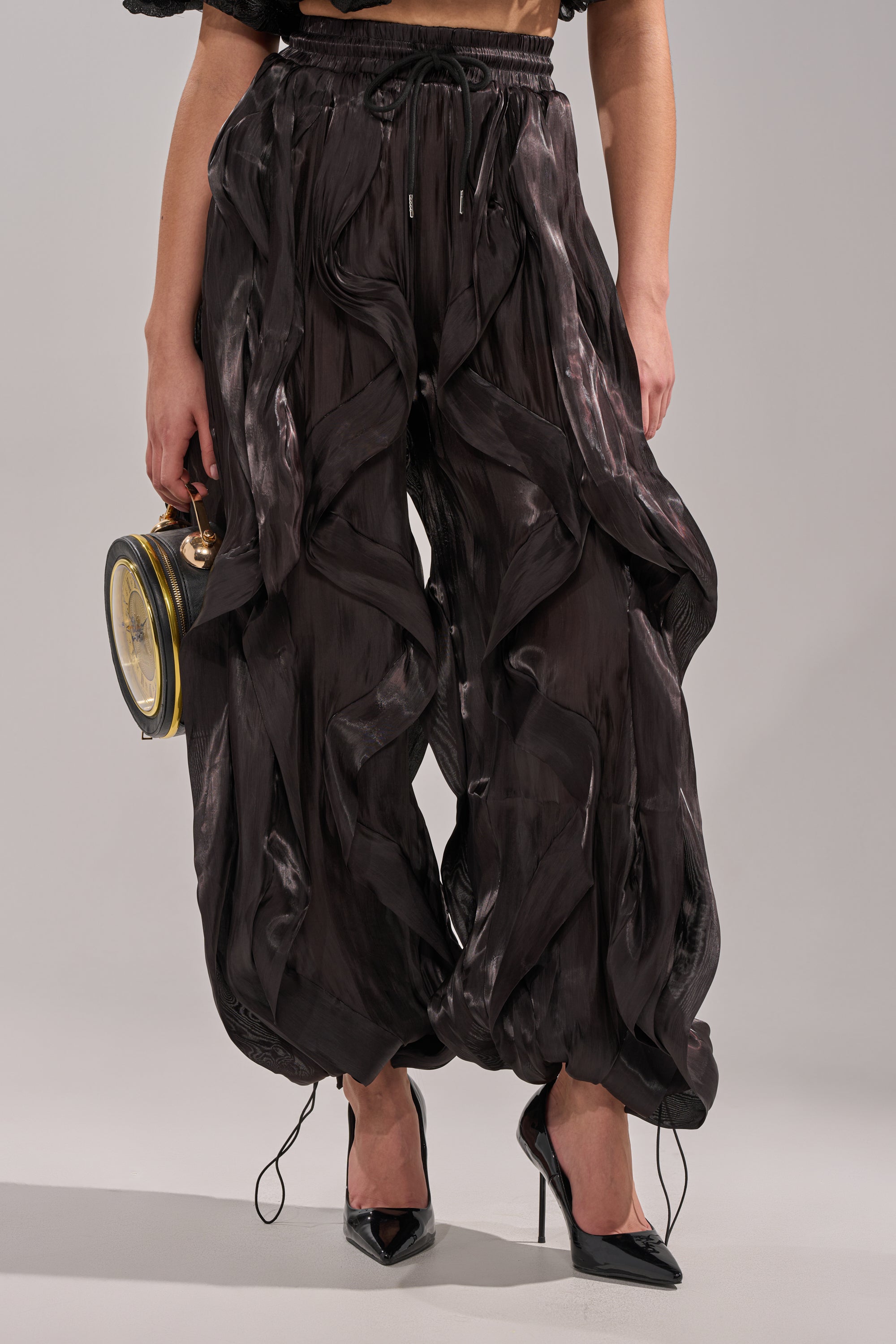 Sporting the COOLEST ON THE BLOCK JOGGER—black, voluminous, and textured with gathered details—paired with black high heels and a round black and gold handbag. The cropped shot highlights this avant-garde street style ensemble. 7