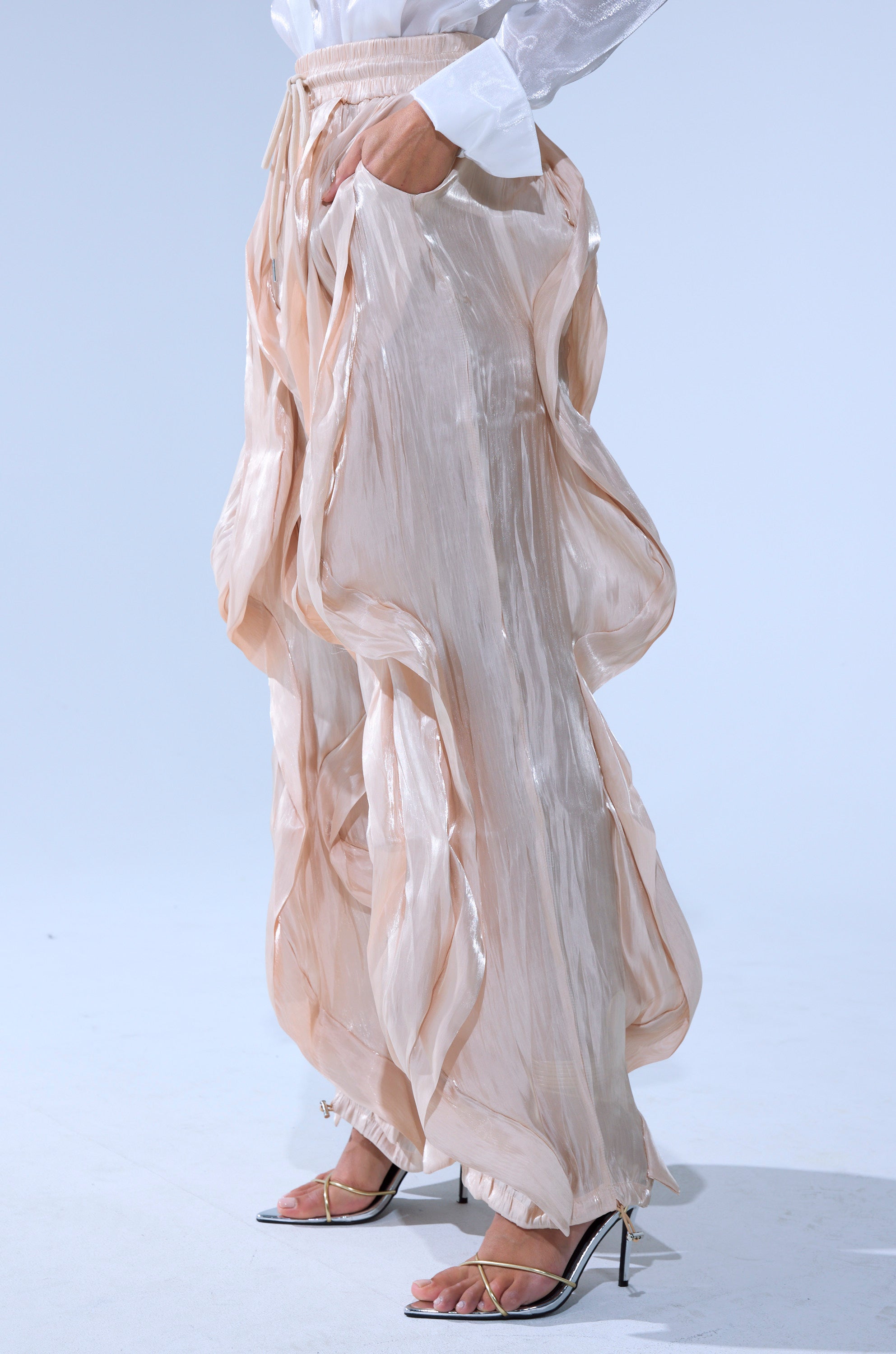 Wearing the COOLEST ON THE BLOCK SATIN JOGGER in loose peach, paired with a white blouse and silver high heels, a person stands against a light background.