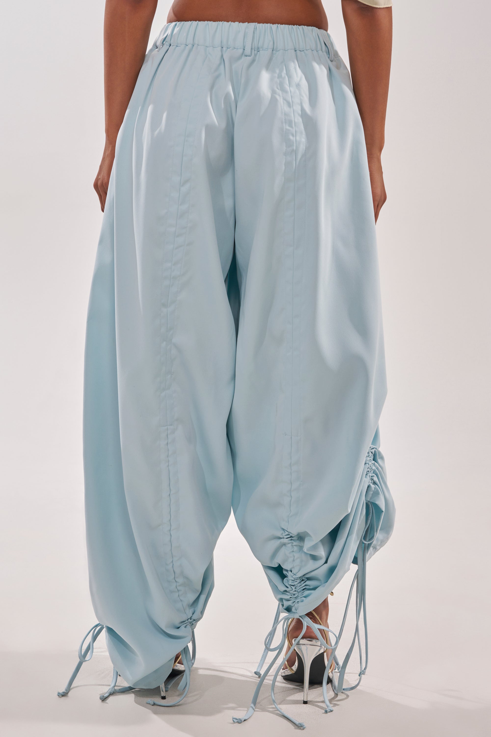 The lower half of a person is shown standing against a plain light background, wearing the DRAMA RUCHED JOGGER IN BLUE with adjustable drawstring ruching at the ankles. 6