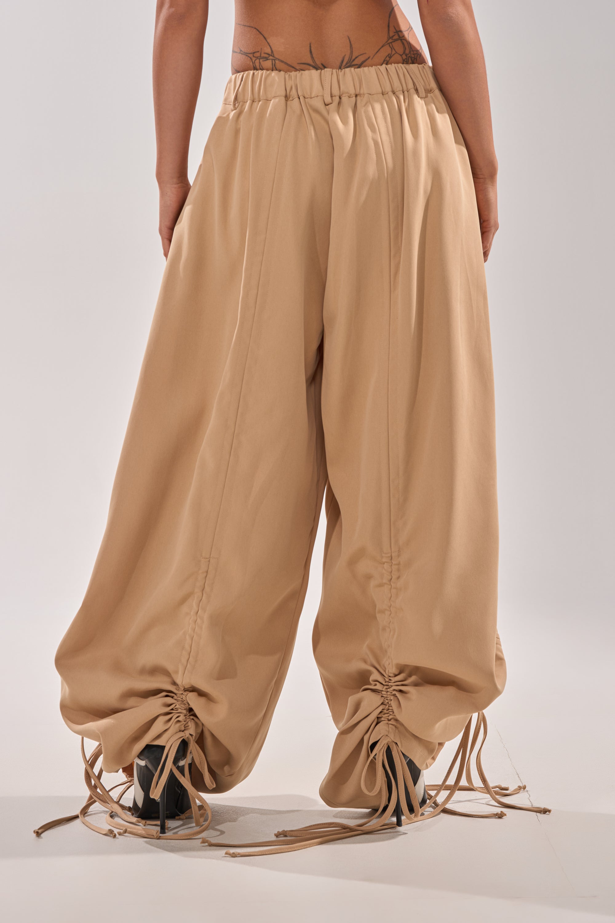Wearing the DRAMA RUCHED JOGGER IN KHAKI, featuring a high-rise elastic waistband and gathered ankles, this person flaunts tattoos on their lower back and arms, capturing an effortless street style vibe. 6