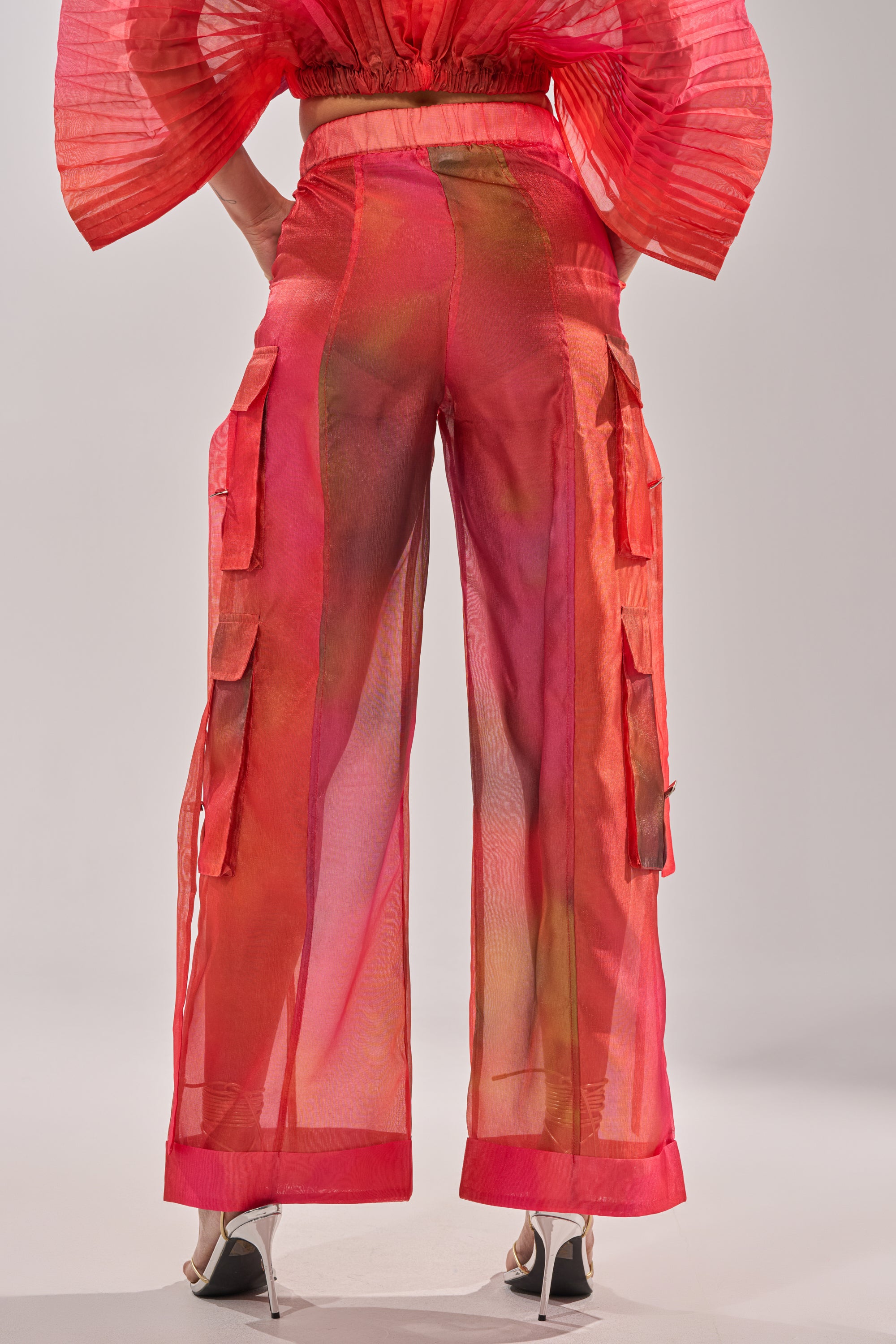 A person is seen from the back wearing STAINED RED LIGHTWEIGHT CARGO PANT—sheer, red chiffon pants with a wide-leg silhouette and large side pockets—paired with high heels, highlighting the pants' flowy, transparent fabric. 4