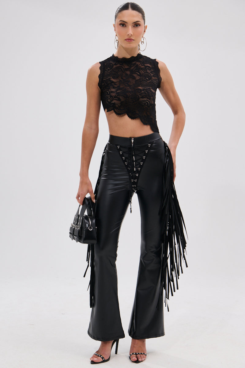 A woman faces forward wearing a black lace sleeveless crop top, SHOW TIME FAUX LEATHER FLARE PANT WITH LACE UP, black high-heeled sandals, and holding a small black handbag for a cowgirl-chic finish.