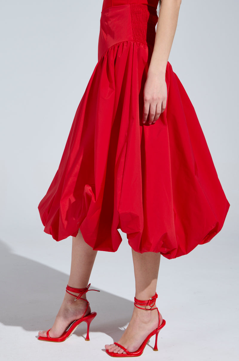 The image showcases a person in the I Found You Drop Waist Midi Skirt in Red paired with elegant red high-heeled sandals. It highlights the skirt's vibrant fabric and stylish footwear against a plain background, focusing on the lower half of the body.