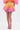A person models the SHELBY OMBRE MINI SKIRT, a puffy bubble hem mini that fades from yellow to pink, paired with a matching crop top and pink strappy heels, standing against a plain white background.