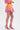 A person stands in profile, wearing a Shelby Ombre Mini Skirt with balloon-style shorts and pink high-heeled sandals, set against a plain white background.