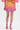 A person stands facing away, wearing the SHELBY OMBRE MINI SKIRT with a bubble hem in a yellow-to-pink gradient and matching pink high-heeled sandals against a plain white background.