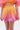 A person wearing a Shelby Ombre Blouse and the SHELBY OMBRE MINI SKIRT with a bubble hem, in a yellow-to-pink gradient, stands against a plain light background.