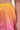 A close-up of a person wearing the SHELBY OMBRE MINI SKIRT, featuring a bubble hem and an elastic waistband with ombre colors fading from yellow to orange to pink. One arm is visible beside the skirt.