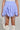 A person is wearing the DREAMERS BUBBLE SKIRT in light blue and white stripes, featuring adjustable drawstrings for a ruched effect. They’re accessorizing with a white handbag and have on white lace-up knee-high boots, all while highlighting a chic, high-rise fit.