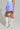 Dressed in the DREAMERS BUBBLE SKIRT featuring blue and white stripes with ruching detail, a person stands against a neutral background wearing knee-high white lace-up boots. The emphasis is on the stylish clothing and footwear.