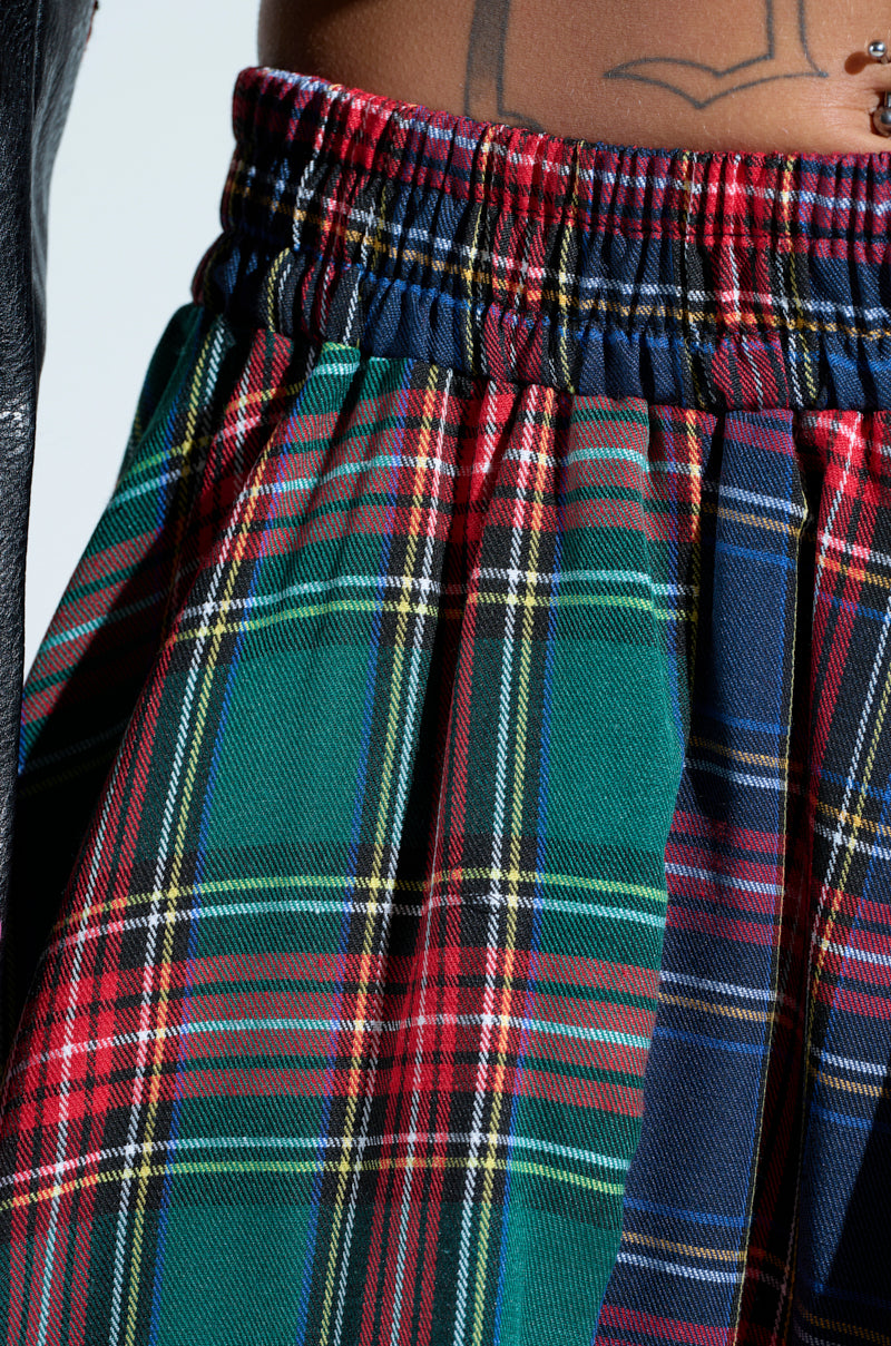 The close-up features the MOVEMENTS PLAID MIDI SKIRT, displaying red, green, blue, and yellow tartan plaid. An elastic waistband ensures comfort and a bubble hem adds flair. A black leather jacket is visible on the left edge.