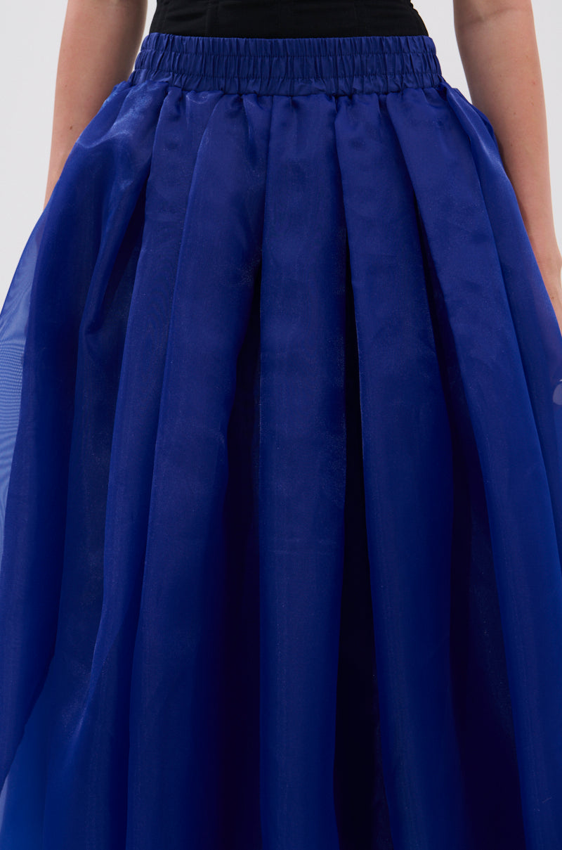 Model wears the STAY CLOSE TO ME MIDI SKIRT IN BLUE, featuring a royal blue pleated design, black waistband, and sheer chiffon overlay, shown from the waist down. 7