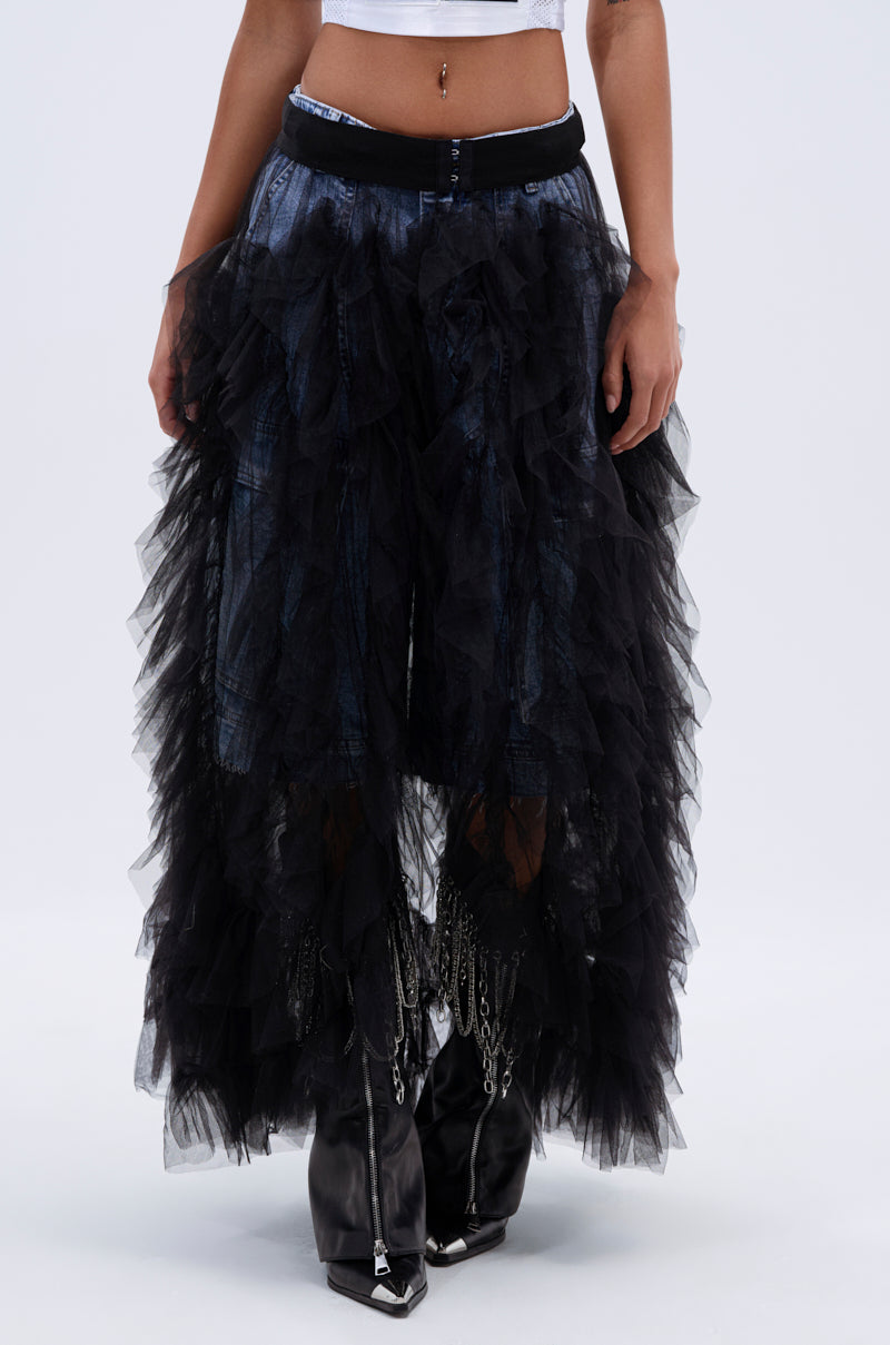 A person wears the DRESSED TO IMPRESS MAXI SKIRT with black tulle ruffle layers over blue jeans, styled with pointed black chain boots. The high-rise fit stands out, with just a glimpse of a sleeveless top visible.