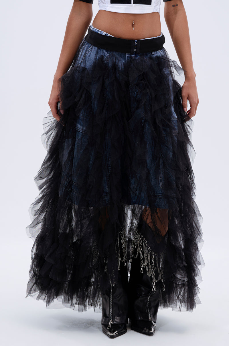 A person wearing the DRESSED TO IMPRESS MAXI SKIRT over denim pants with chain details, plus black pointed boots and a cropped white top, stands against a plain light background.