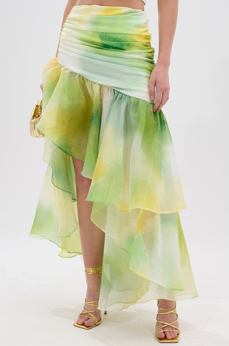 A person wears the LIMONE CHIFFON MIDI SKIRT in light green and yellow with an asymmetrical silhouette and ruched waistband, paired with strappy heels and a metallic gold purse. 1