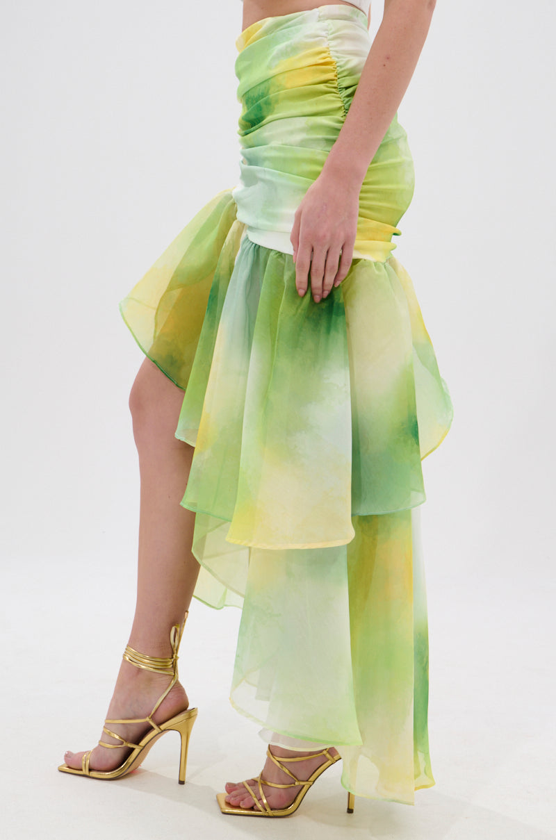 Someone is wearing the LIMONE CHIFFON MIDI SKIRT—a flowing green and yellow ombré chiffon midi skirt with a ruched waistband and asymmetrical silhouette—paired with gold strappy high heel sandals, against a plain white background. 2