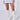 A model stands against a white background wearing the QUEEN OF LOVE DISTRESSED MINI SKIRT IN WHITE, featuring an asymmetrical silhouette and high-waisted design. Her legs are adorned with knee-high white lace-up heeled boots, creating a delicate yet edgy style.