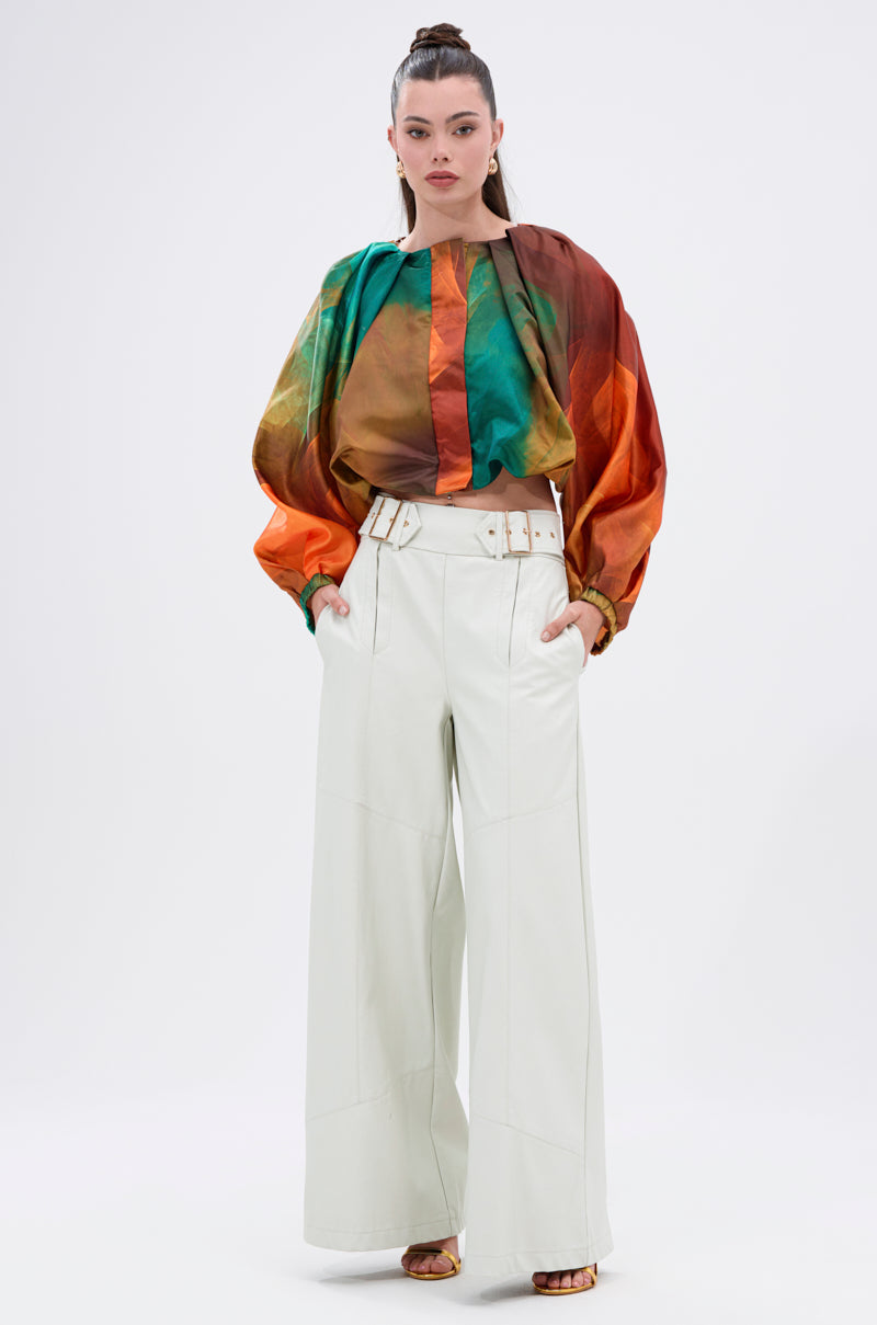 A woman stands against a plain background wearing the TIFFANY OMBRE BLOUSE with balloon sleeves, tucked into high-waisted, wide-leg white pants with a matching belt and beige open-toe heels.