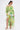 A woman styles the LIMONE CHIFFON BLOUSE, featuring an off-the-shoulder neckline, sheer puff sleeves, and a green-yellow-white watercolor print. Its ruched waist and flowy design pair perfectly with gold heels and her chic ponytail.