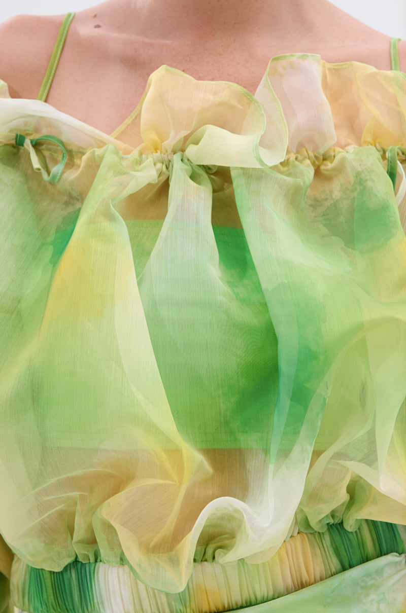 Close-up of a person wearing the LIMONE CHIFFON BLOUSE, a light, sheer top in green, yellow, and white with ruffles, gathered neckline, and puff sleeves for a soft, airy look. 7