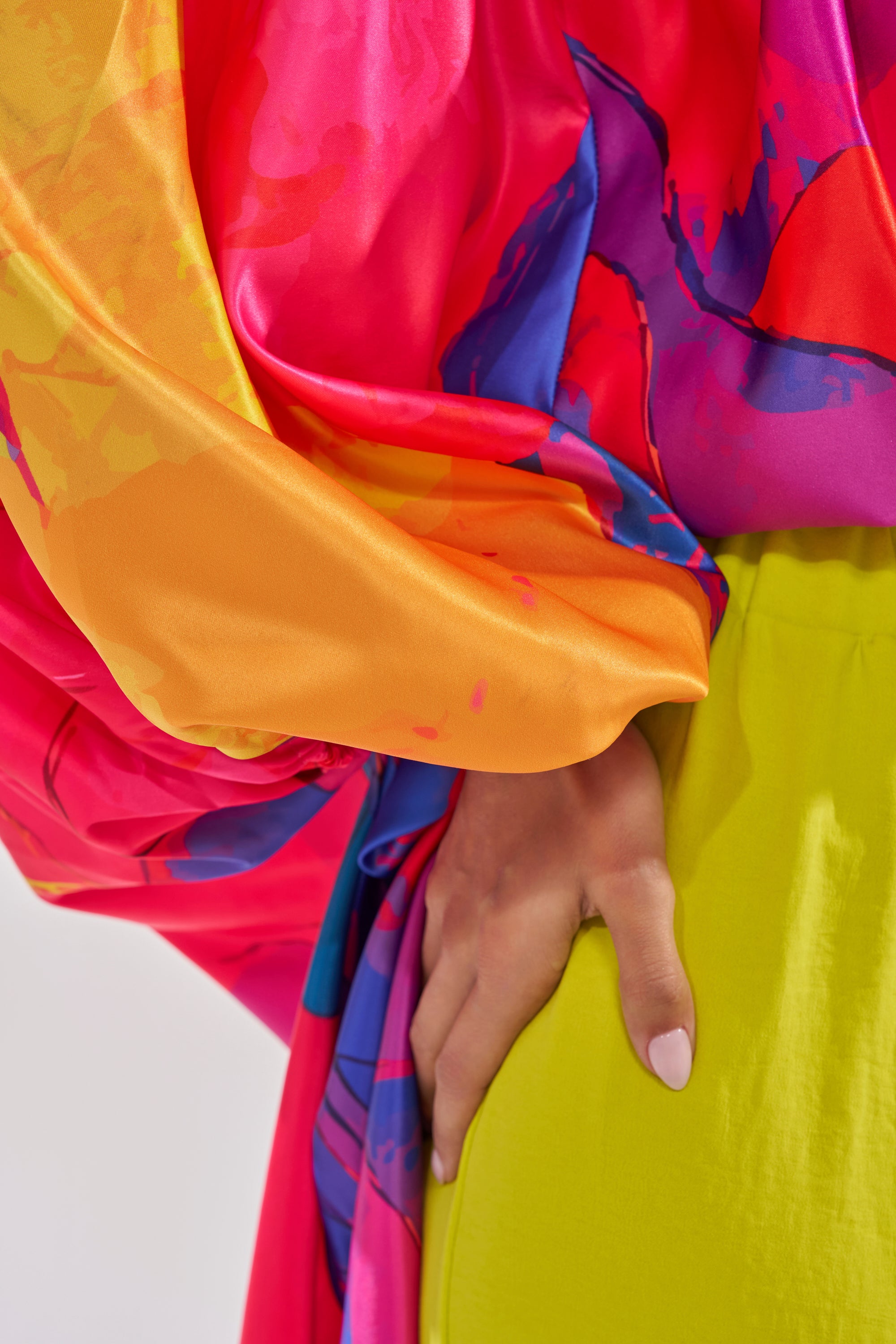 Wearing the BE WITH ME BLOUSE, a vibrant off-shoulder top with pink, orange, and blue patterns, and yellow pants, a person rests their hand on their hip, highlighting bold vacation style. 5