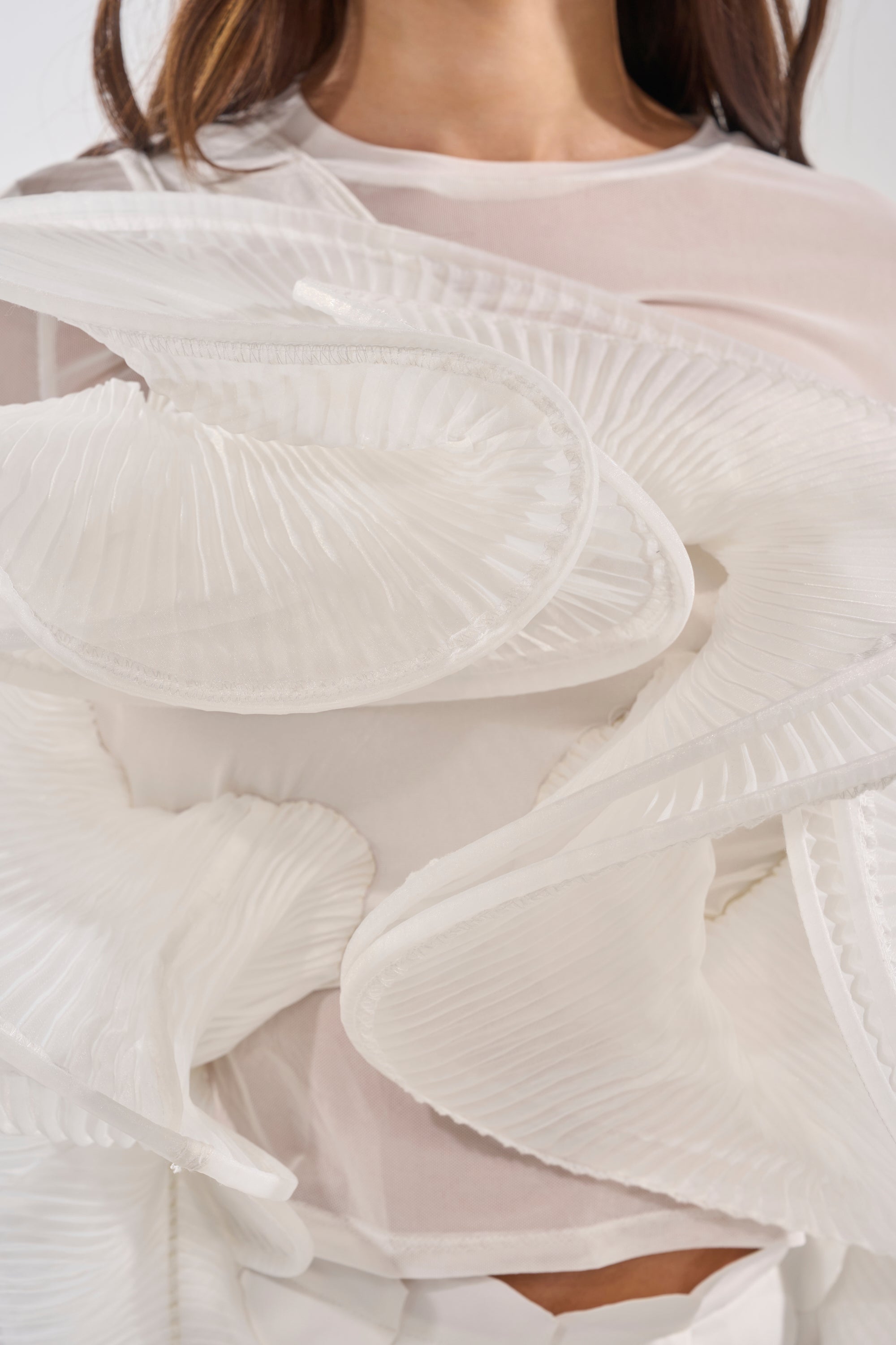 A close-up of a woman wearing the DRAMA RUFFLE BLOUSE, featuring sheer white fabric with bold, sculpted pleated ruffles that form a dramatic, abstract design. 5