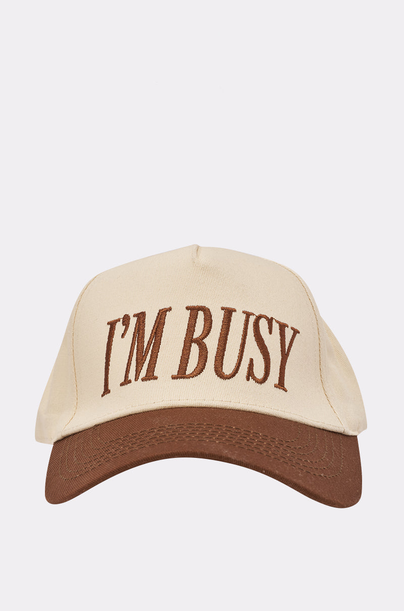 The I REALLY AM THO BASEBALL HAT features a beige color block design, brown brim, and "I'M BUSY" embroidered in large brown letters on the front. Adjustable snapback closure for a custom fit.