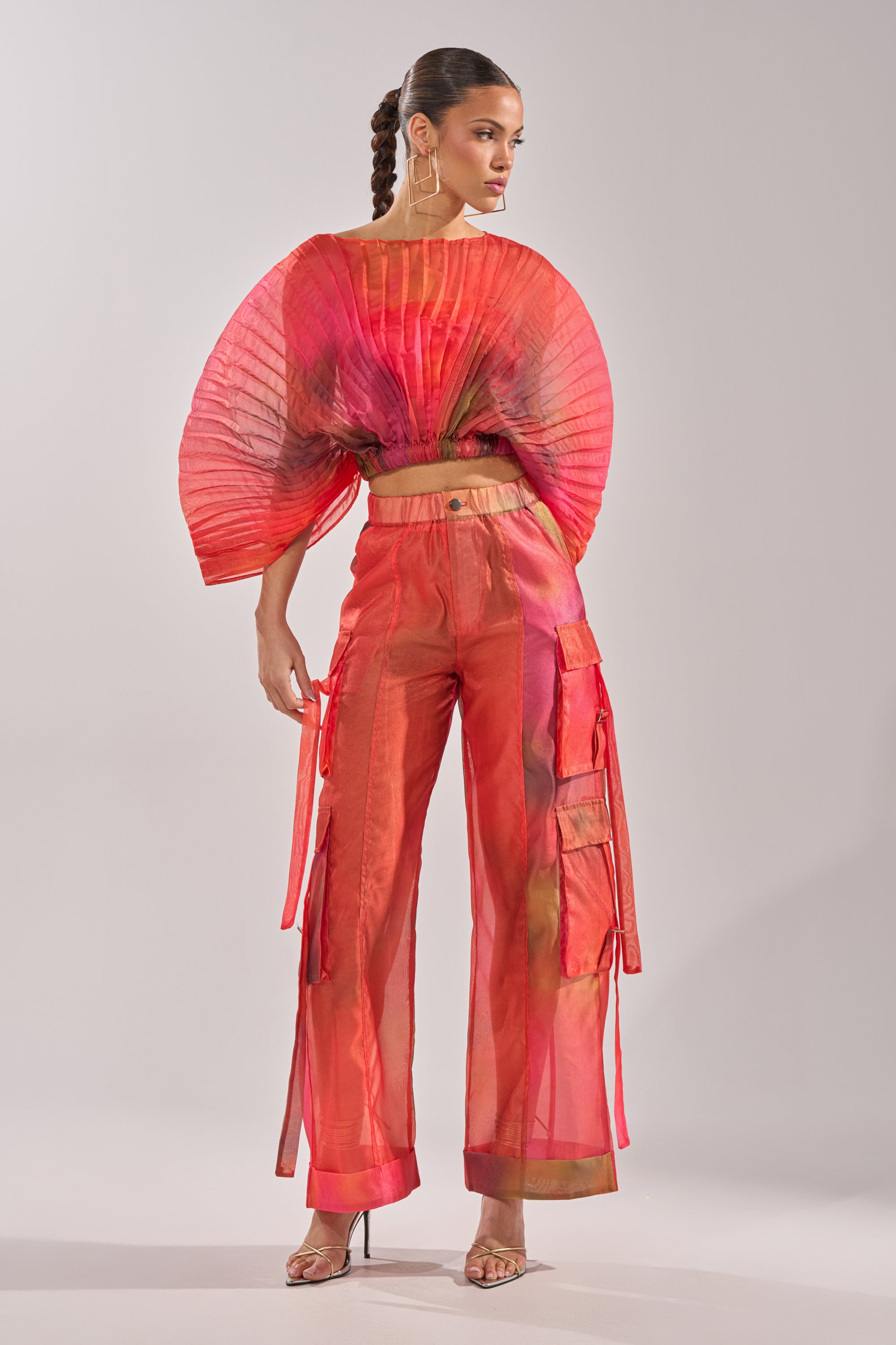 A woman sports a bold look with the STAINED RED CROPPED BLOUSE, sheer red wide-leg cargo pants, hoop earrings, a sleek braided hairstyle, and high heels. 6