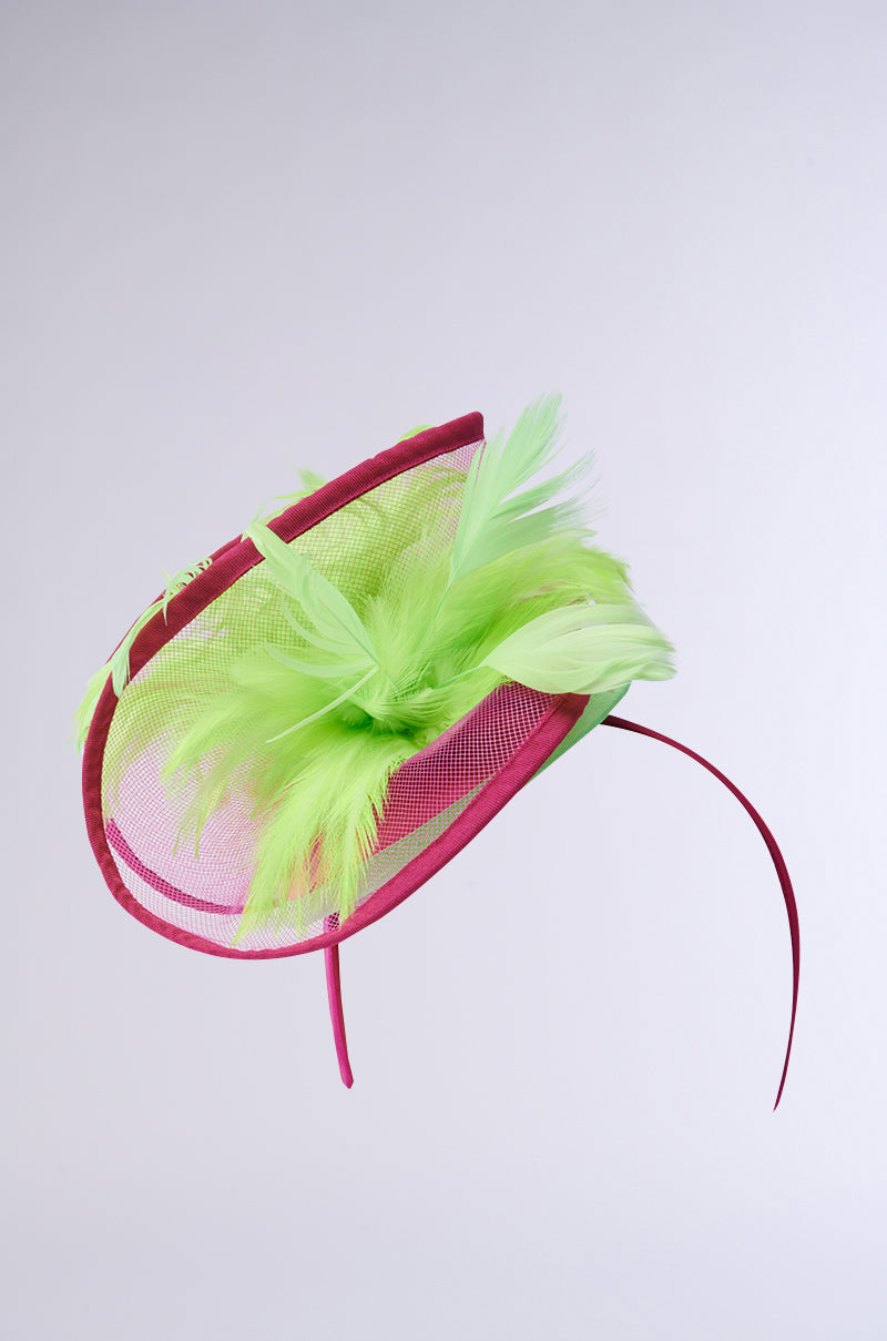 The TO THE DERB FASCINATOR is a vibrant maximalist piece with a bright pink base and airy green feathers. Designed with elegant curves and a thin headband, this bold hair accessory makes a lively statement, perfect for any occasion. 2