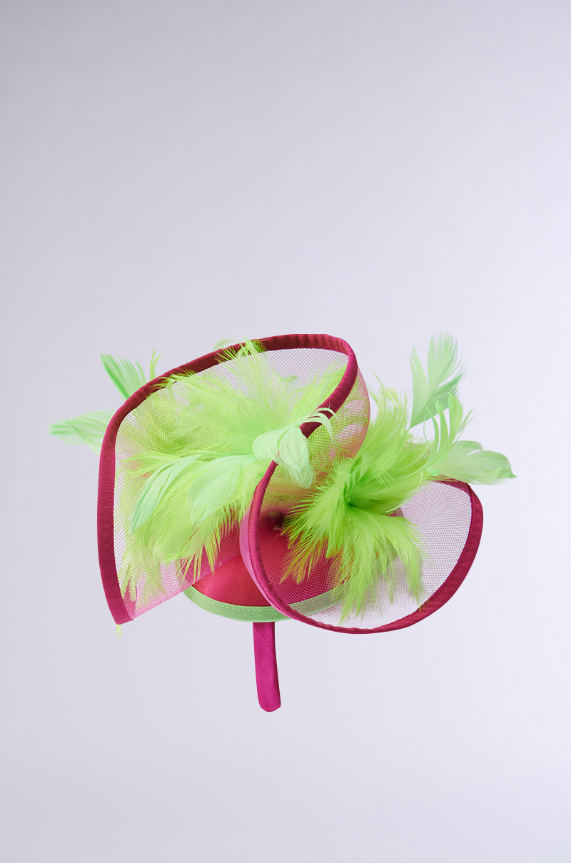 The TO THE DERB FASCINATOR features a vivid fuchsia base with bold green feathers, a sculptural twist design, and a matching fuchsia headband—all set against a light gray background, perfect for the maximalist enthusiast. 3