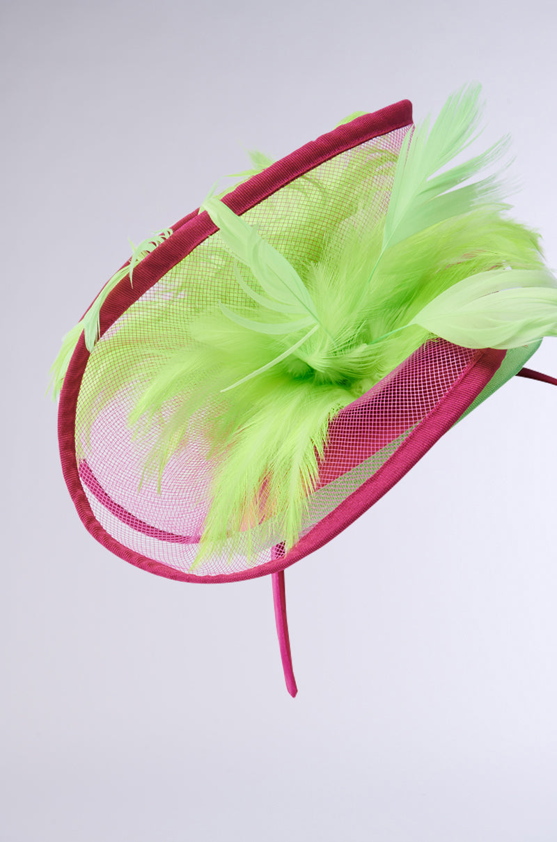 The TO THE DERB FASCINATOR features a vibrant, maximalist design with lime green feathers and pink mesh on a maroon headband. Its asymmetrical style creates a striking, modern look against neutral gray, making this hair accessory truly stand out. 4