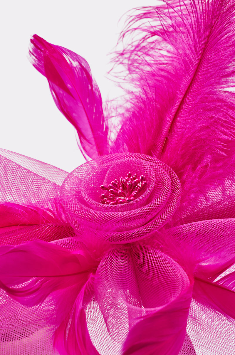 Close-up of the DERBY DAY PINK FASCINATOR featuring vibrant hot pink mesh, a netted flower centerpiece, decorative beads, and large feather accents against a light background. 5