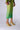 A person wearing a green, translucent, rhinestone-studded midi dress paired with AZALEA WANG HUGHIE LIME SANDAL yellow flared stiletto heel sandals. They are holding a beaded clutch bag. The image captures the person from the shoulders down, standing against a plain background.