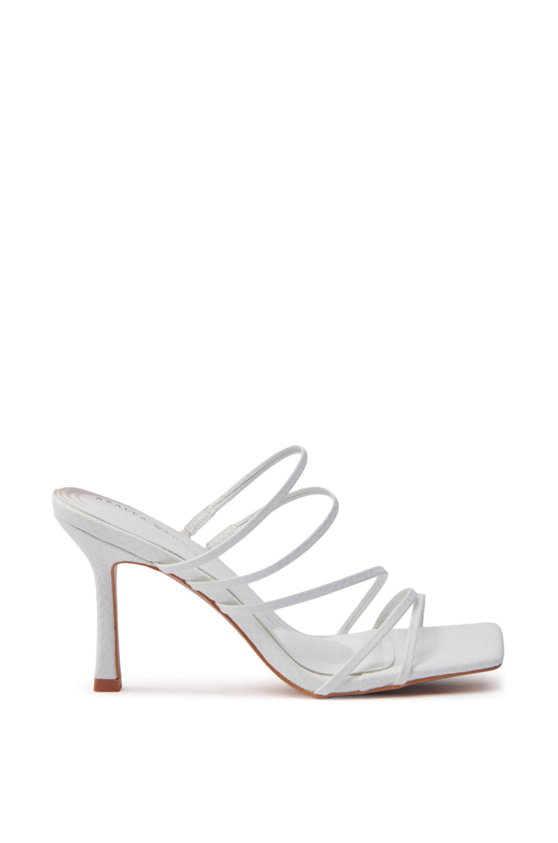The AZALEA WANG HUGHIE WHITE SNAKE SANDAL is a white, heeled sandal featuring a square toe and multiple thin straps, crafted from vegan leather. It boasts a chic stiletto heel and is shown in side view on a plain white background.