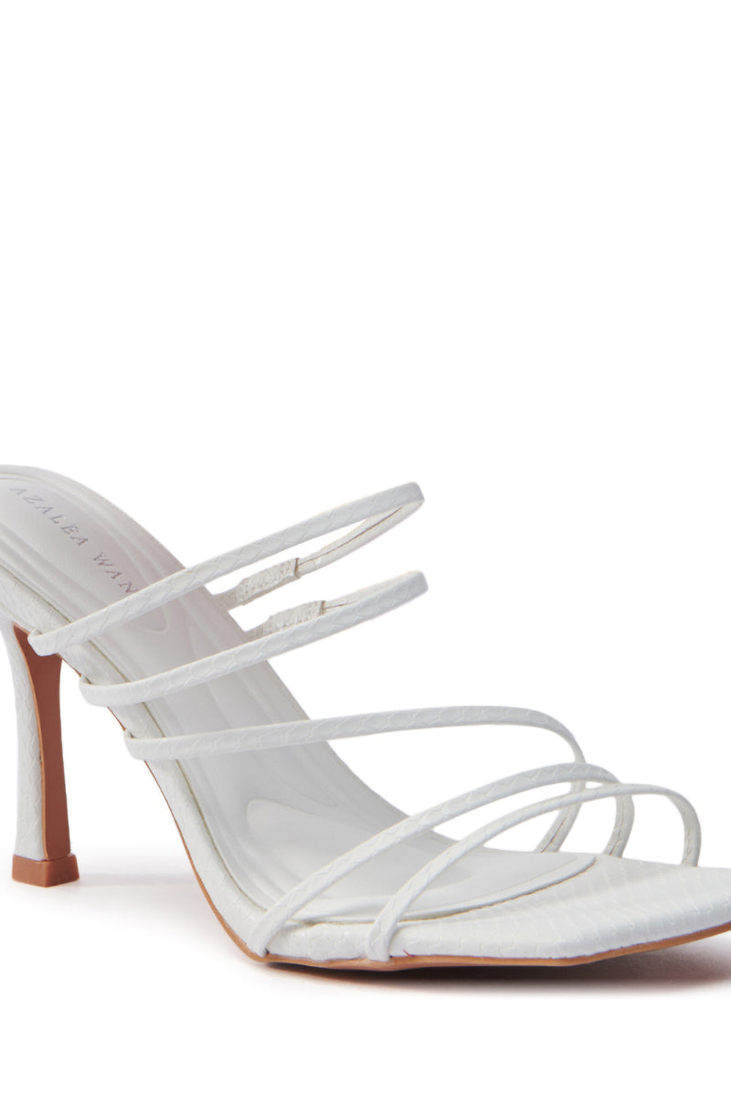The AZALEA WANG HUGHIE WHITE SNAKE SANDAL features a single white high heel with a slender, slightly curved stiletto and multiple delicate straps over the foot. Made from vegan leather, this elegant sandal is presented against a white background.