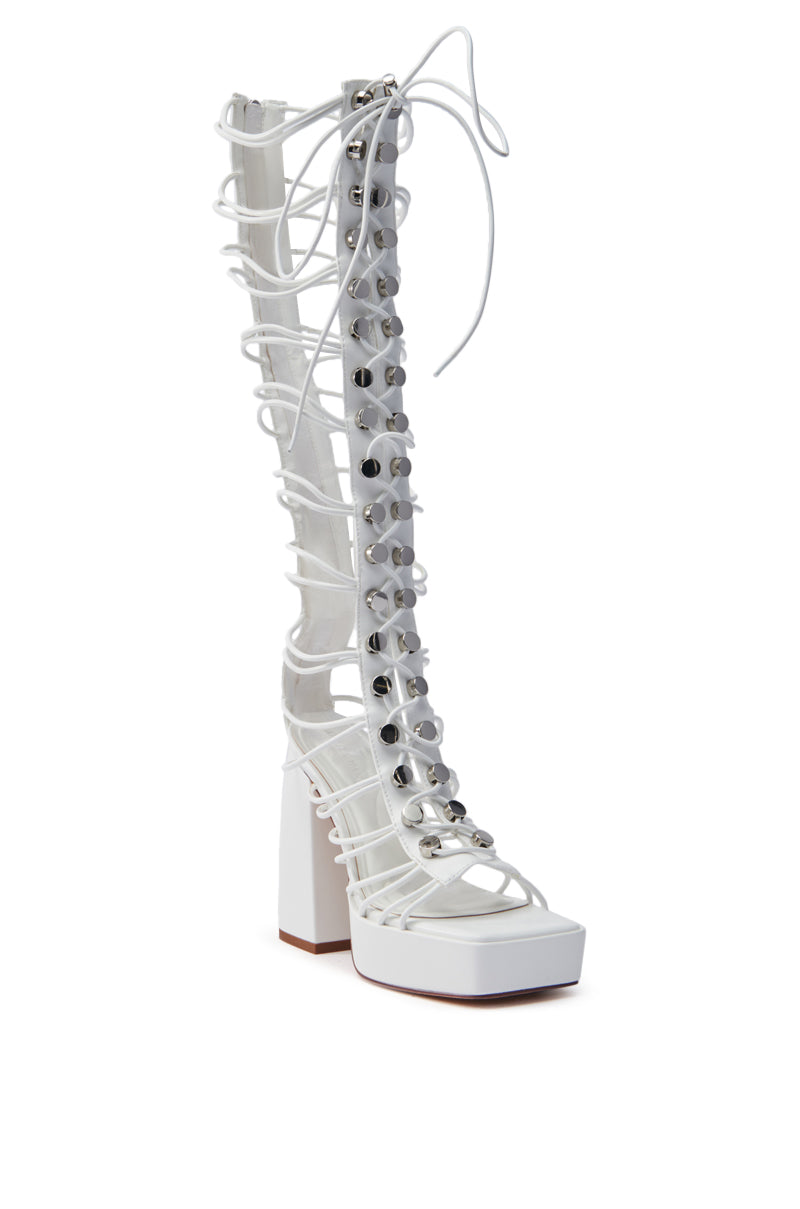 The AZALEA WANG HUYEN White Gladiator Sandal is knee-high with a chunky block heel, vegan leather straps in a lattice design, metallic studs along the front, and laces at the top.