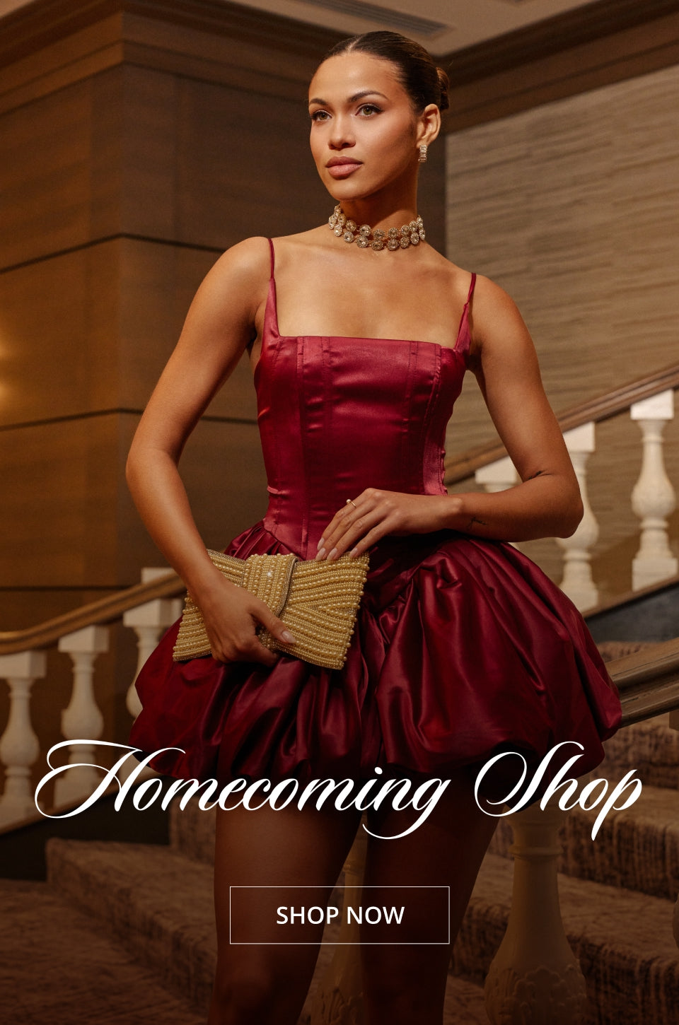 A woman wearing a burgundy satin mini dress with thin straps and a voluminous skirt, holding a woven clutch, posed on an indoor staircase with 'Homecoming Shop' and 'SHOP NOW' text overlays.