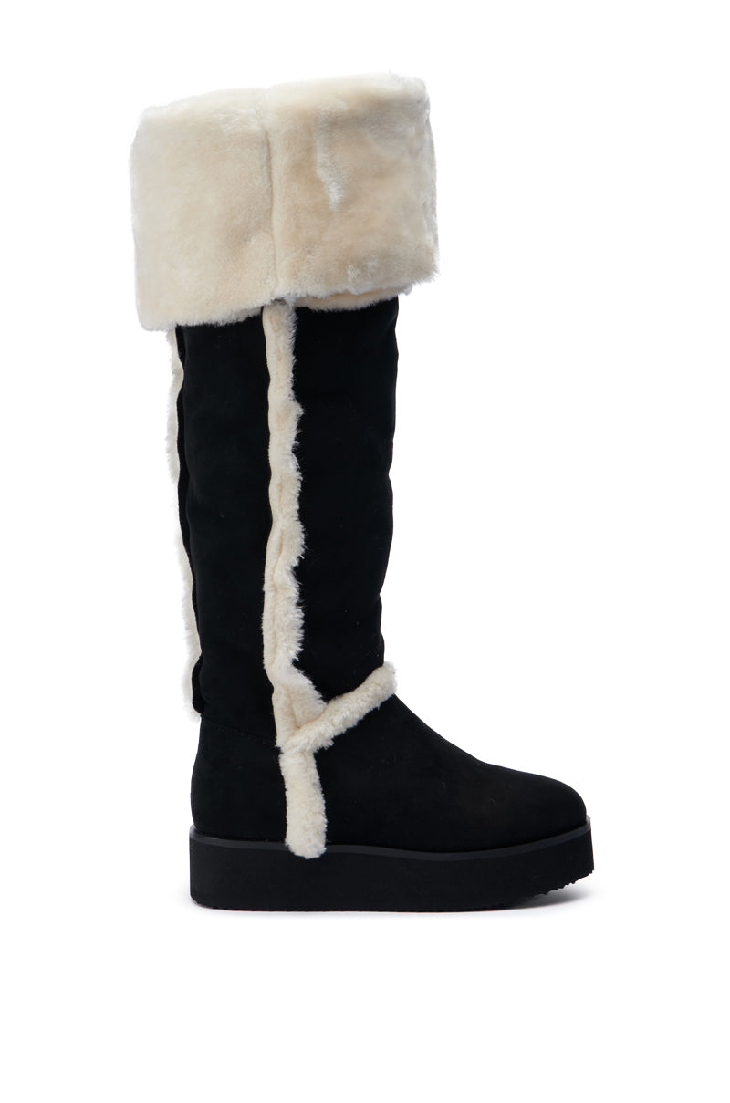 The AZALEA WANG ICELANDER BLACK FUR BOOT is a tall thigh-high black suede boot featuring a thick cream-colored fur trim at the top and along the seams. It has a chunky black sole and a folded-over design near the top, offering a cozy winter look.