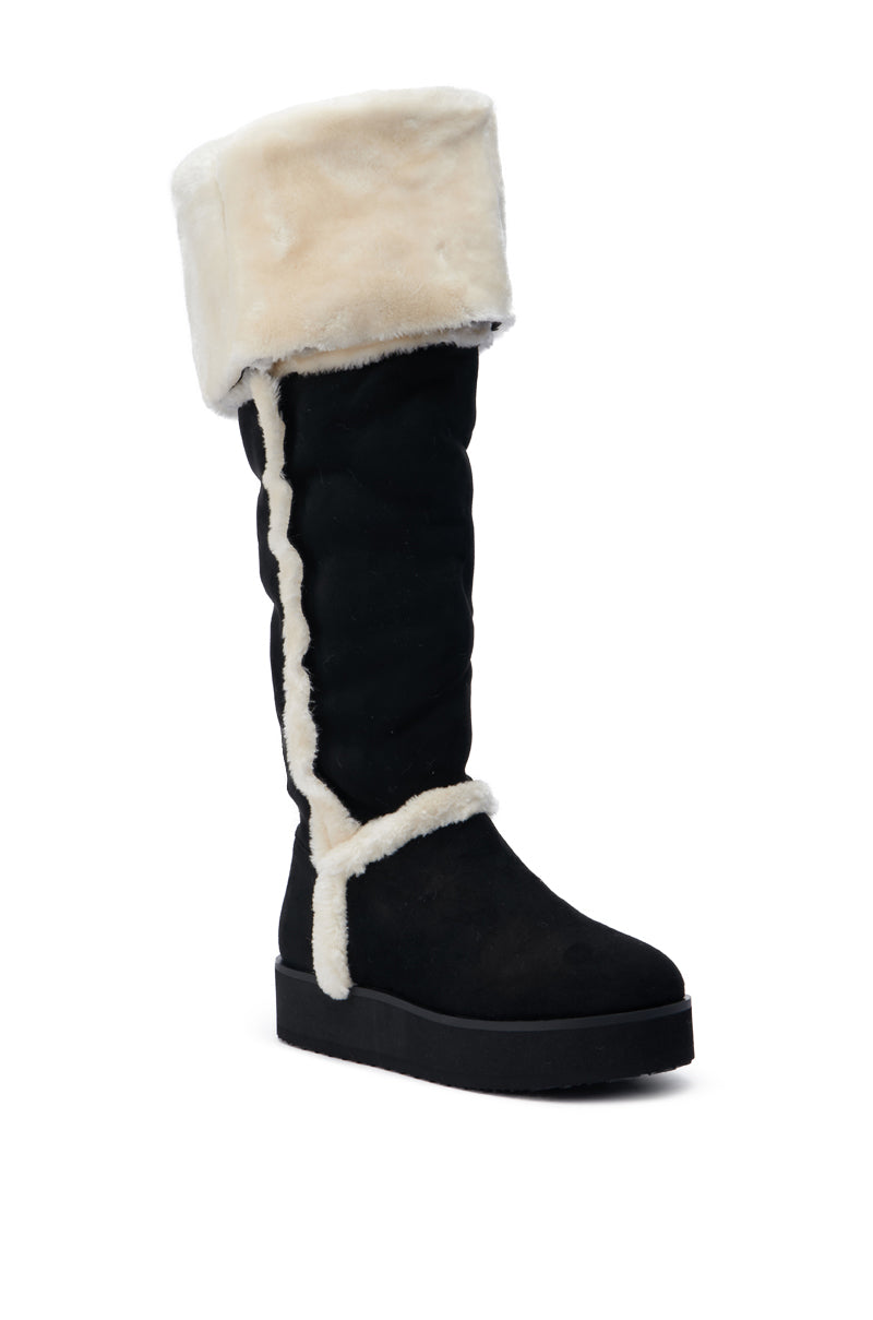 The AZALEA WANG ICELANDER BLACK FUR BOOT is a stylish thigh-high faux suede boot in black, featuring a thick, fluffy cream-colored fur cuff and trim that runs down the side and around the ankle. It sits on a black sole and is angled to the left, highlighting its plush, cozy design.