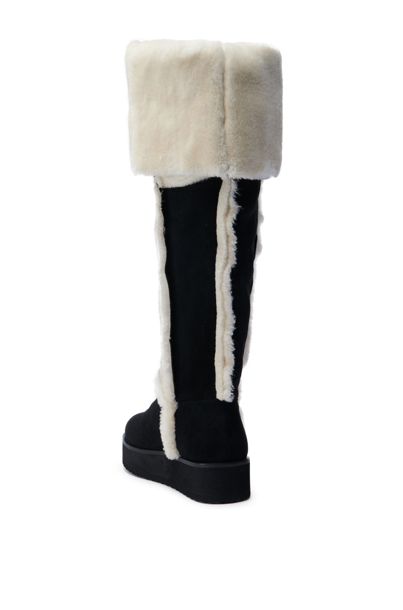 The AZALEA WANG ICELANDER BLACK FUR BOOT features a black, faux suede design with a contrasting thick white fur cuff and trim, seen from the back. This knee-high boot has a flat sole, with plush fur elegantly complementing the sleek material for a chic appearance.