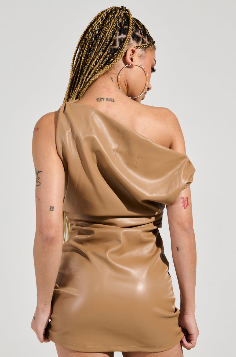 A woman with braided hair is seen from the back wearing the curve-hugging UNREACHABLE FAUX LEATHER MINI DRESS, featuring an asymmetrical cowl neckline. She showcases multiple tattoos on her arms and back while complementing her look with large hoop earrings.