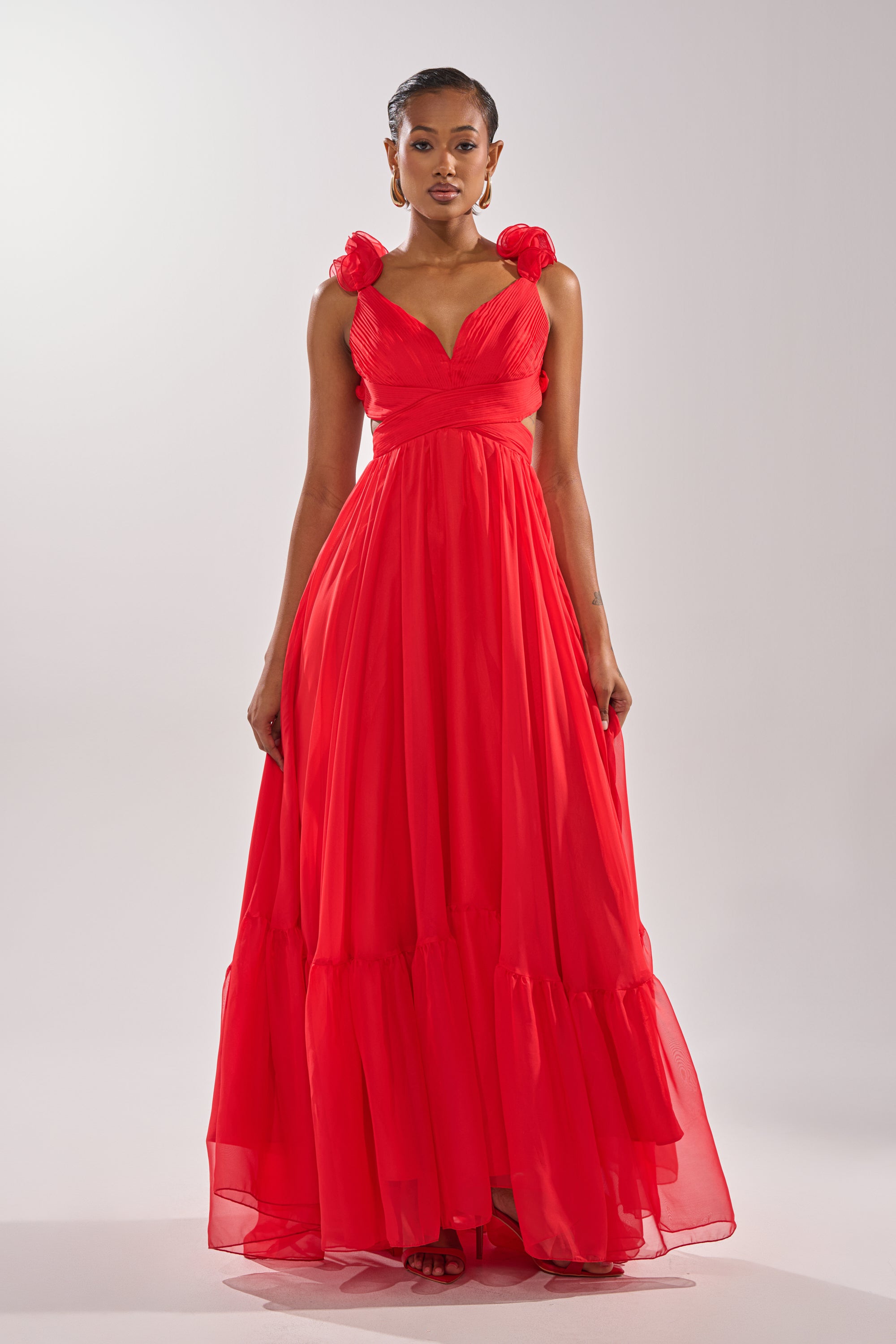 A woman wears the DREAM GIRL MAXI DRESS IN RED, featuring floral-embellished shoulder straps and a ruffled hem—an elegant special occasion dress—posed against a plain light background. 2