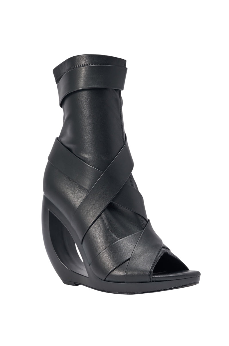 The AZALEA WANG IGNITE BLACK WEDGE OPEN TOE BOOTIE features wide belting details, a unique empty wedge heel, black faux leather material, and an open toe design for a modern look. 3